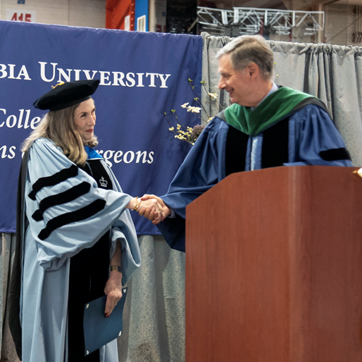 The dean of the Vagelos College of Physicians and Surgeons shaking the hand of a PhD graduate at commencement.